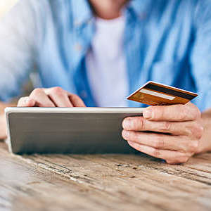 Shot of an unrecognizable man doing online shopping on his digital tablet and holding his credit card while being seated at a table.