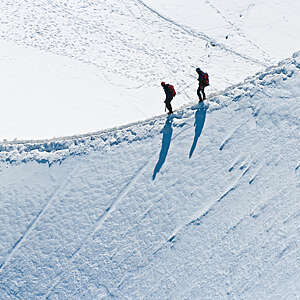 Alpinists roped together to climb along a narrow snow arete in bright sunshine high on Mont Blanc in the French Alps.
