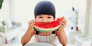 Asian little girl eating a slice of watermelon at home.