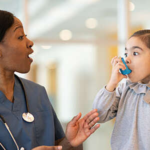 Female doctor playfully teaches a small asthmatic girl to use an inhaler.